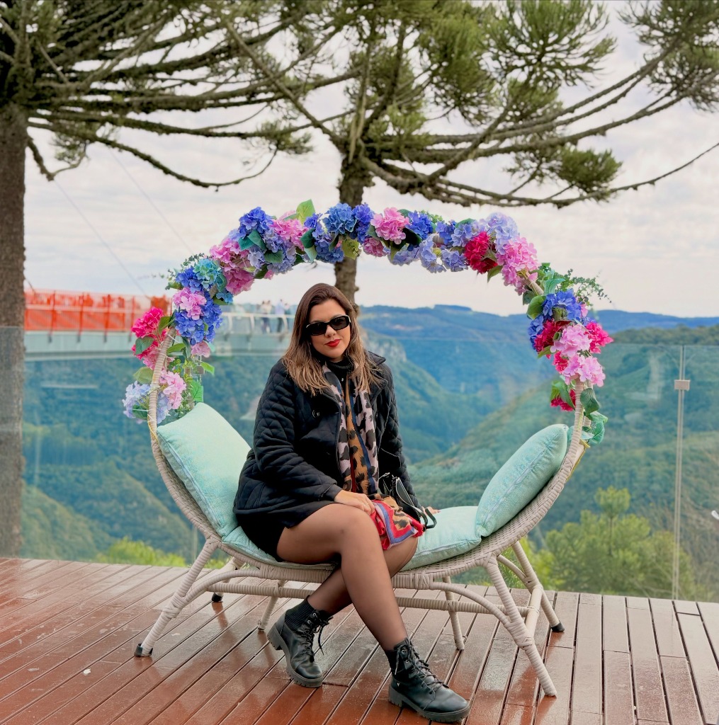 Mulher no balanço de flores com araucárias e montanhas ao fundo